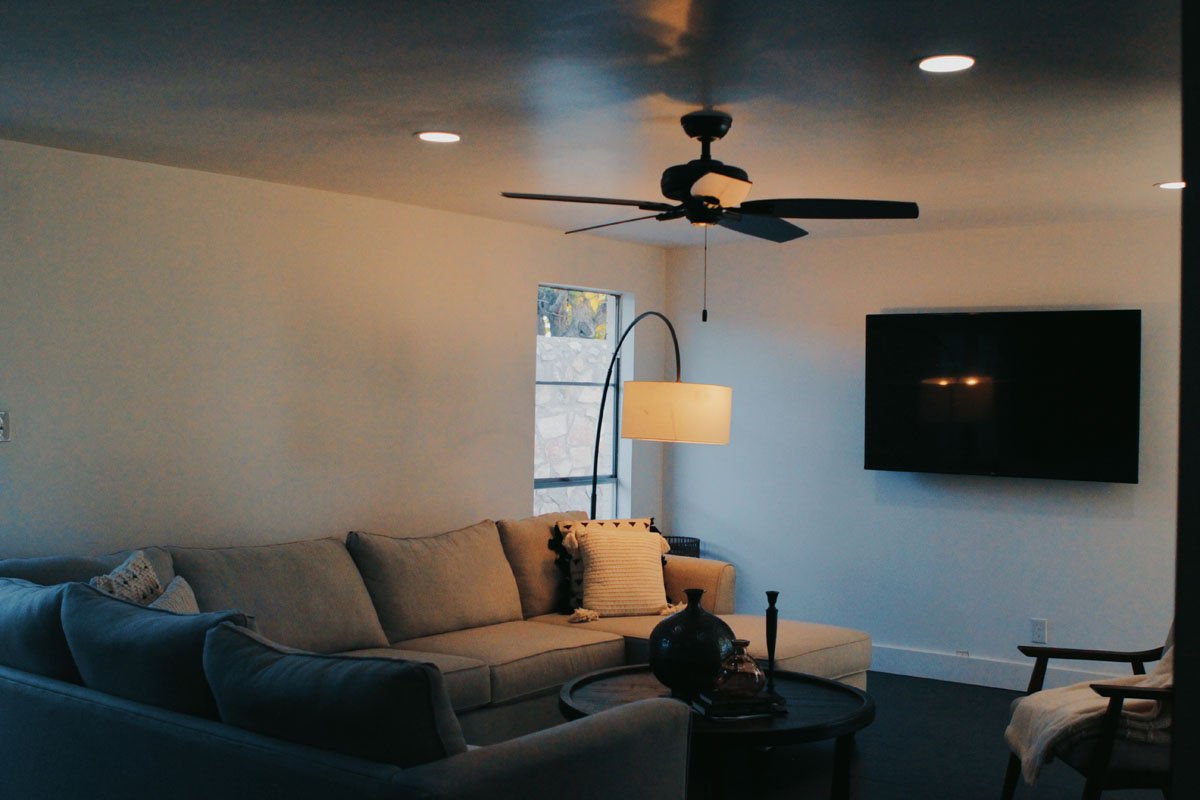 A dimly lit living room with two couches, a lamp, a ceiling fan, and a tv
