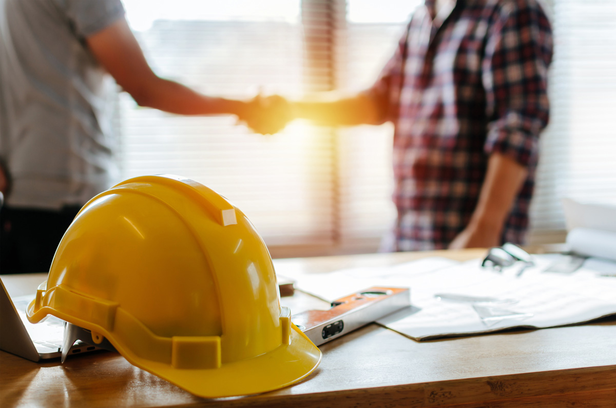 Two people shaking hands behind a yellow hardhat on a desk in El Paso.